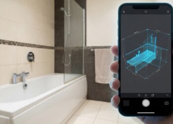 Main tenant un smartphone qui scanne une salle de bains pour en relever les cotes.