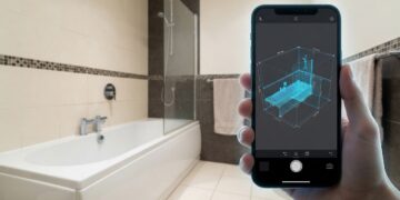 Main tenant un smartphone qui scanne une salle de bains pour en relever les cotes.